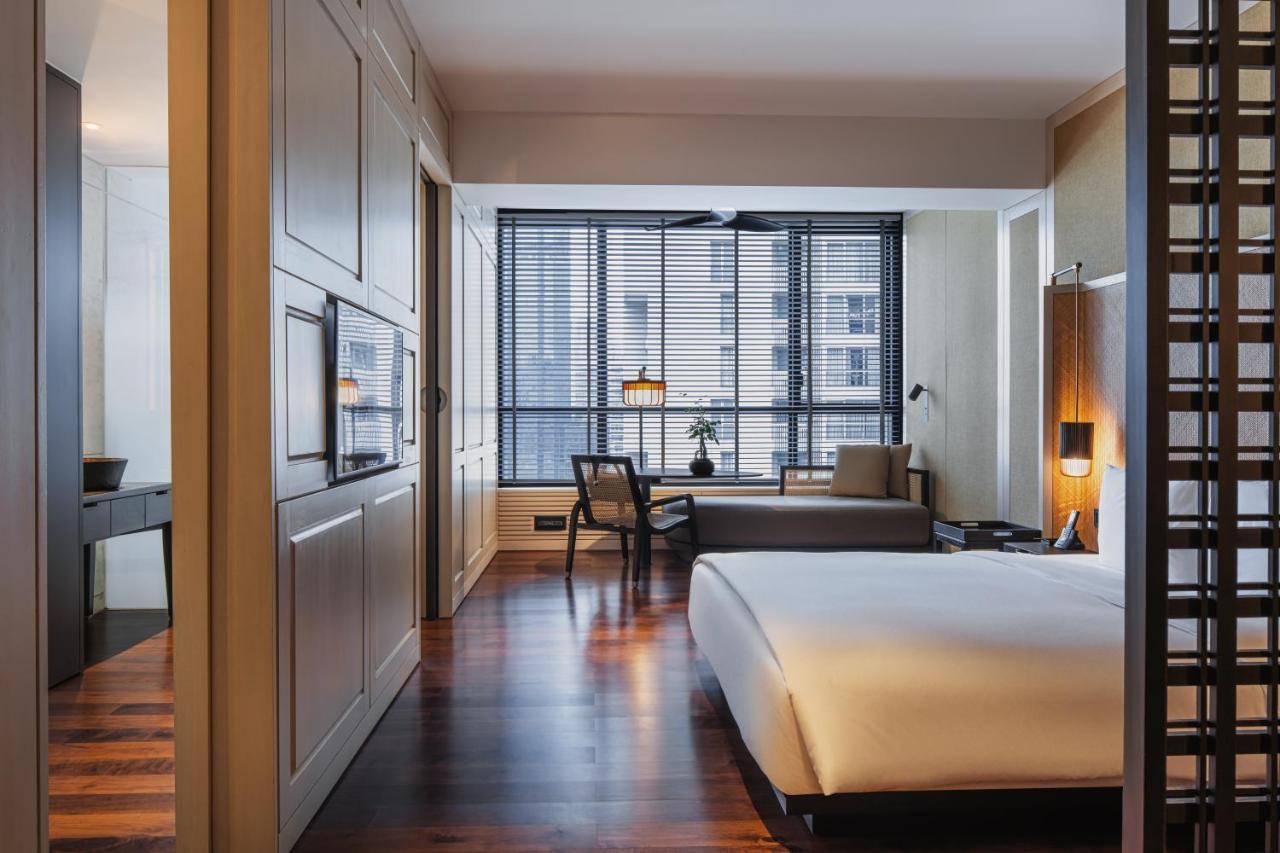 The Ruma Hotel And Residences Kuala Lumpur Kültér fotó The photo shows a modern hotel room with a clean and minimalist design. The room features a large bed with white bedding positioned against a wall. There is a wooden floor that adds warmth to the space. A sitting area is visible in the background, fe
