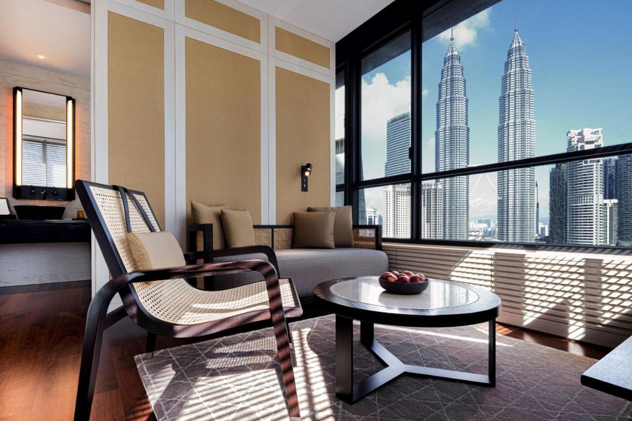 The Ruma Hotel And Residences Kuala Lumpur Kültér fotó The photo depicts a stylish and modern interior of a living space, featuring a seating area with a comfortable chair and a sofa. There's a round coffee table in the center, adorned with decorative items. The room has large windows that offer an impre