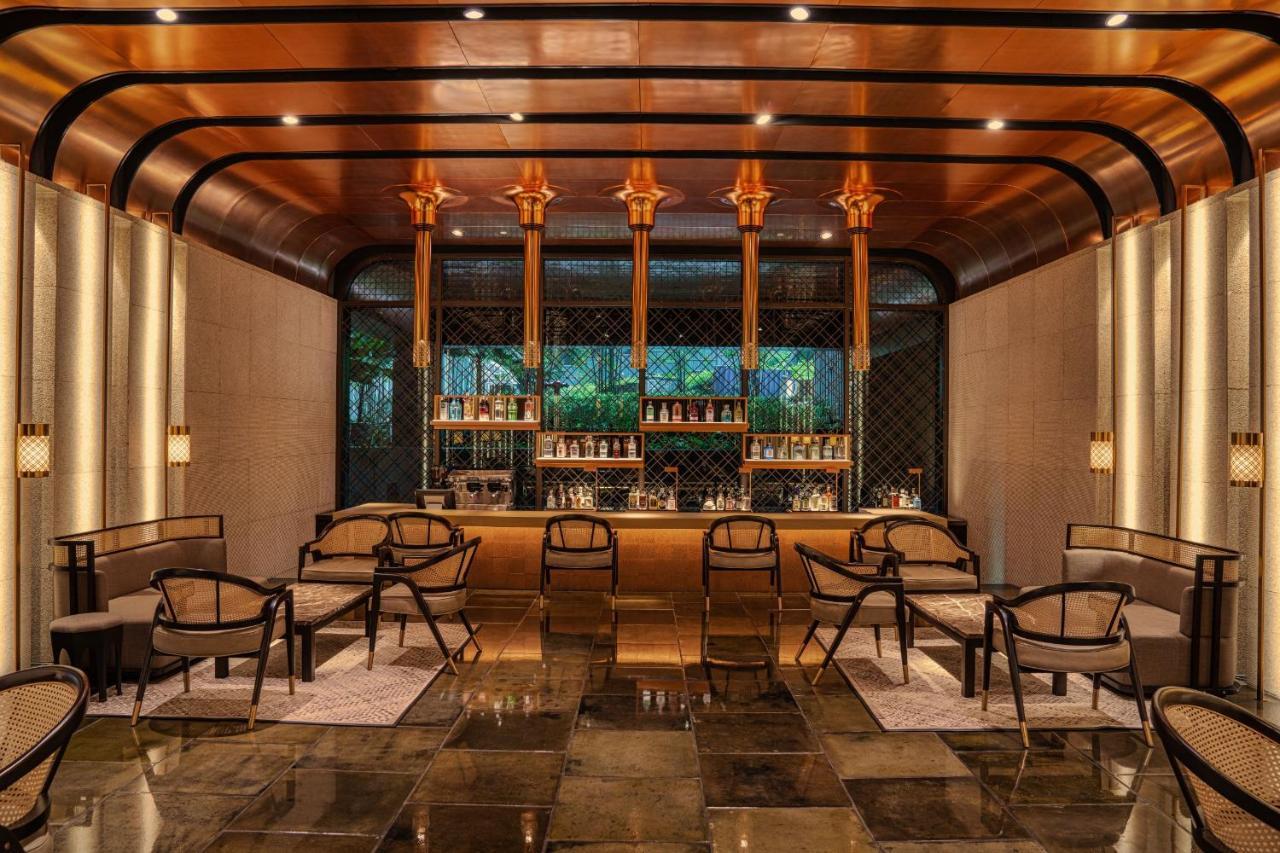 The Ruma Hotel And Residences Kuala Lumpur Kültér fotó The photo shows a stylish interior of a bar or lounge area. The space features a combination of elegant materials, including polished metal accents and warm lighting. A wooden bar counter is centrally located, with several shelves displaying various 