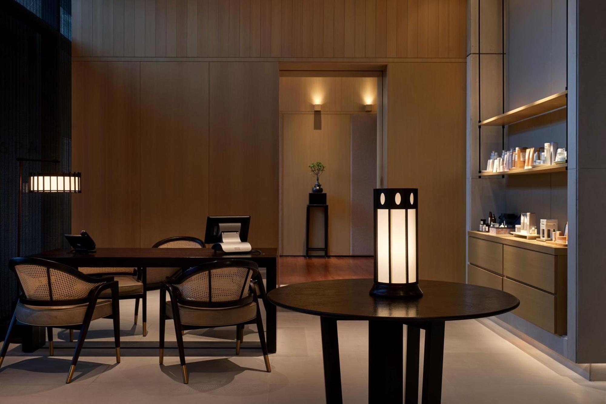 The Ruma Hotel And Residences Kuala Lumpur Kültér fotó The photo shows a modern, minimalist interior space. It features a wooden wall with soft lighting, enhancing a calm atmosphere. In the foreground, there is a round table with a uniquely designed lamp on it. Surrounding the table, there are stylish wo